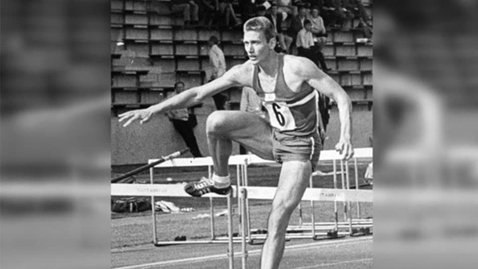 John running and leaping over some hurdles. The photo is in black and white.